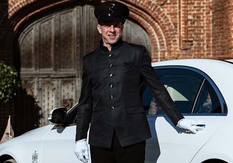Well-dressed chauffeur standing next to a black luxury car, ready for pick-up in Austin.